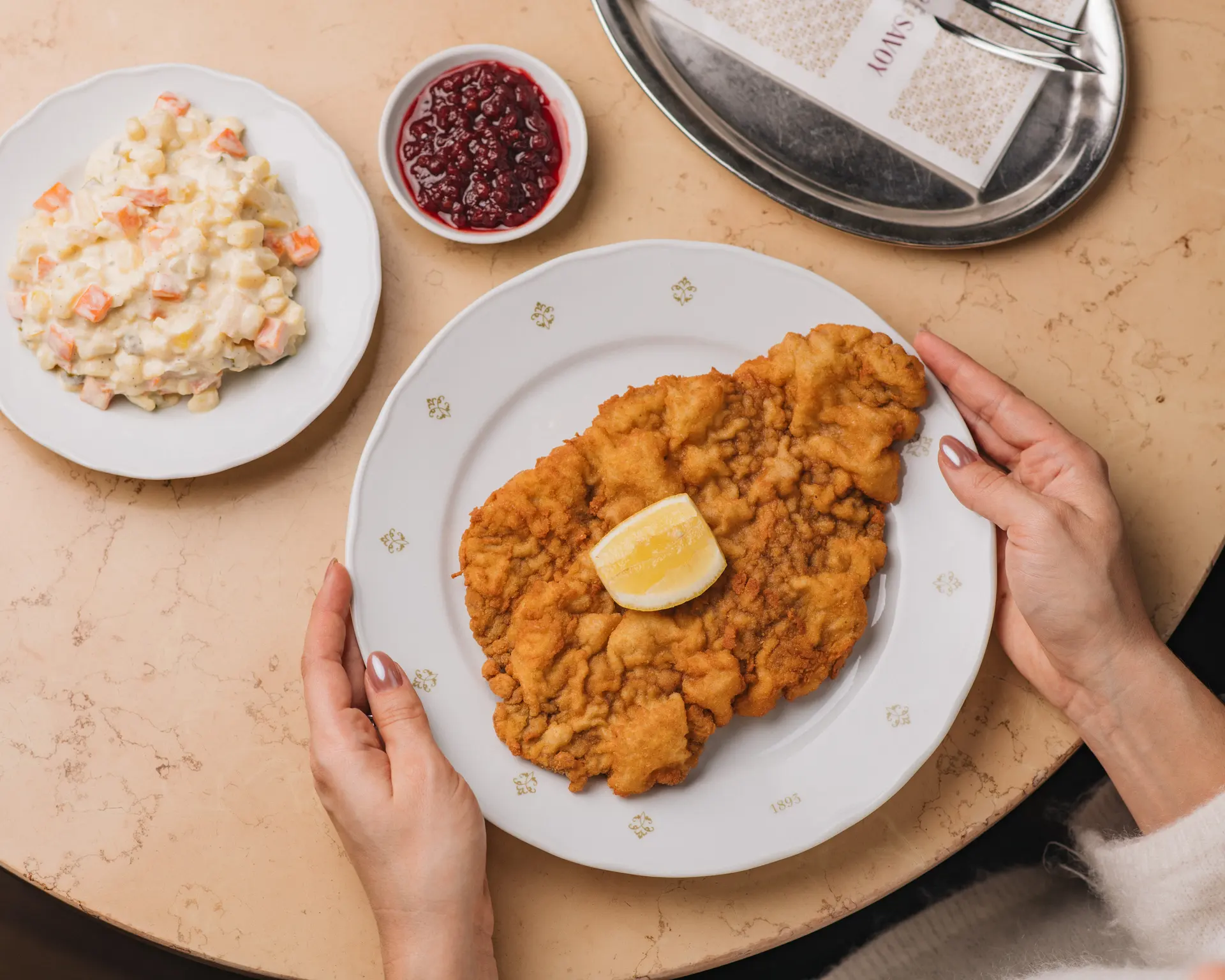 Kuřecí řízek s citronem, bramborovým salátem a brusinkami servírovaný u stolu.
